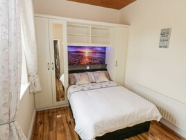 Un dormitorio con cama, armario, una pared con un cartel y ventana con cortinas.
