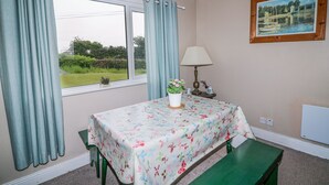 Une pièce avec un lit, une table recouverte d’une nappe à motifs floraux, une lampe, un tableau au mur et une vue sur la verdure à l’extérieur.