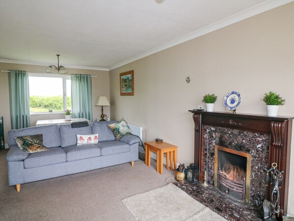 A living room with a grey sofa, a small wooden table, a fireplace, and a window with curtains.
