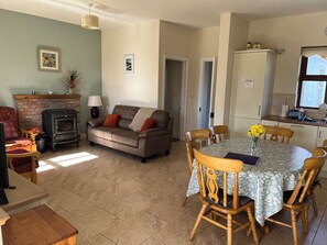 A cozy living room with a fireplace, a dining table with chairs, and a kitchen area. - Cloonkee Cottage (Cloonkee)