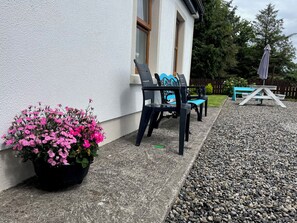 A patio area with a black and blue outdoor chair, a small table, and a potted plant with pink flowers. - Cloonkee Cottage (Cloonkee)
