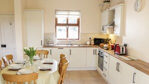 Una cocina con armarios blancos, una mesa de comedor de madera para cuatro comensales y una ventana sobre el fregadero.