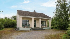 Une maison de plain-pied avec un toit en tuiles, une véranda avec deux chaises et une allée gravillonnée.
