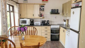 Une cuisine avec des meubles de rangement en bois, une table à manger avec des chaises, un four à micro-ondes, un grille-pain, une machine à café et un réfrigérateur.