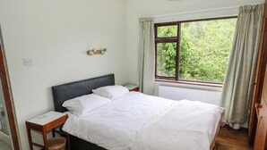Une chambre à coucher avec un lit, des tables de chevet, une fenêtre avec des rideaux et une vue sur la verdure à l’extérieur.