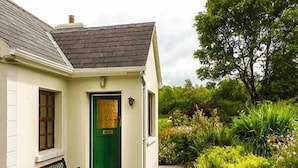 Een charmant huis met een groene deur, een bank ervoor en een tuin vol verschillende planten.