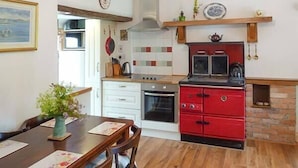 Een keuken met een rode kookplaat, witte kasten en een houten eettafel met stoelen.
