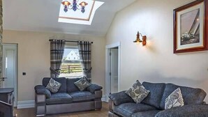 Un salon avec deux canapés, un luminaire au plafond, une fenêtre avec des rideaux et un tableau encadré au mur.