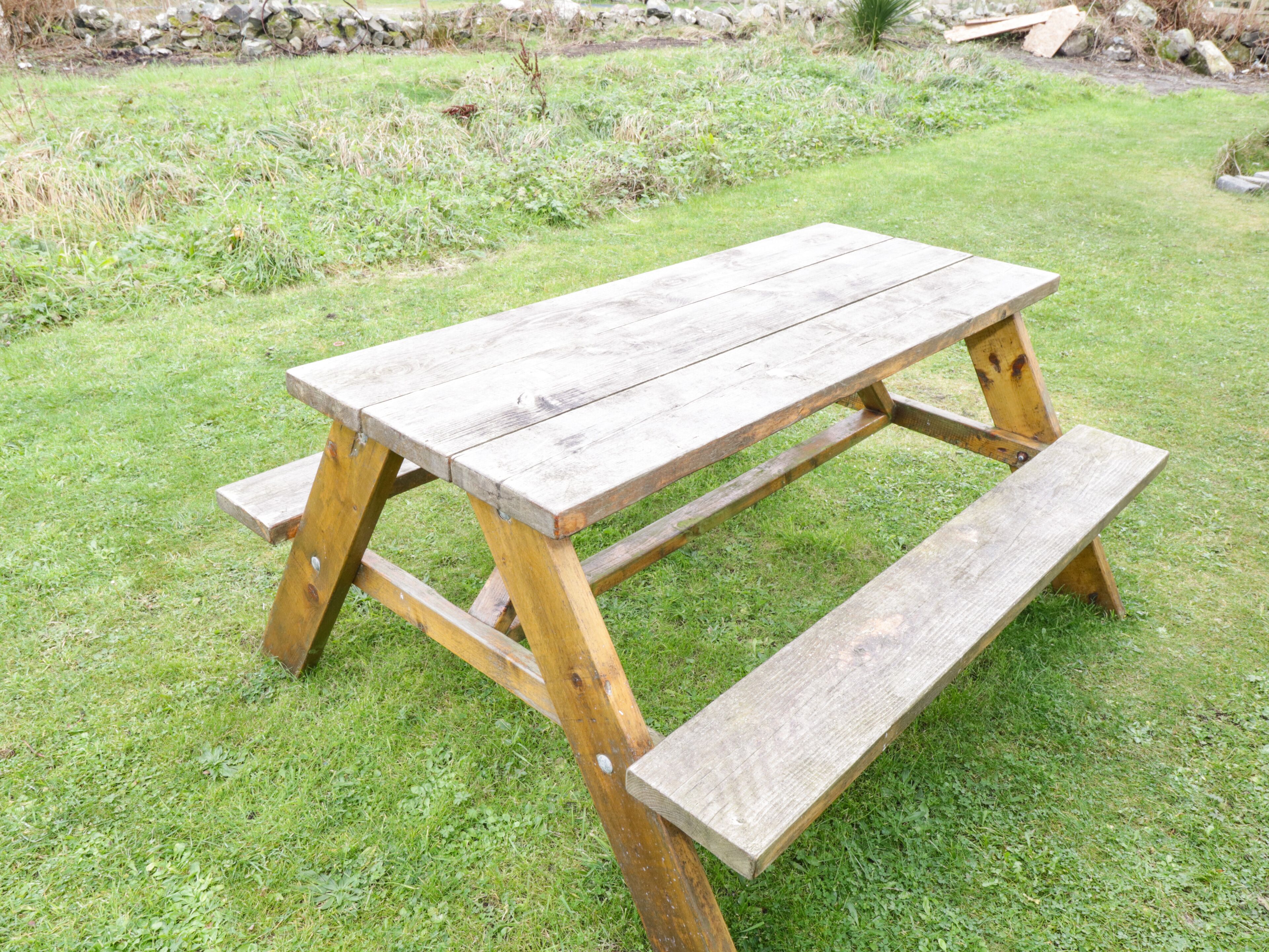 Una mesa de picnic de madera con bancos en un campo cubierto de césped.