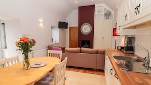 A cozy living room with a sofa, a dining table with chairs, and a kitchen area with a sink and cabinets. - Laharn Cottage (Killorglin)