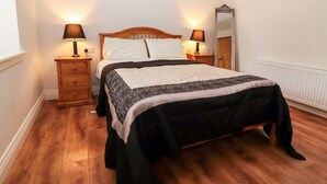 A neatly arranged bedroom with a wooden bed, two bedside tables with lamps, a mirror, and a radiator. - Laharn Cottage (Killorglin)