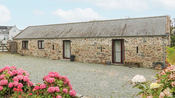 A stone building with a gravel driveway and pink flowers in the foreground. - Swallow's Nest (Tacumshane)