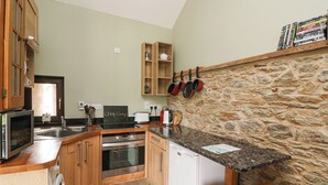 A compact kitchen with wooden cabinets, a stone wall, a built-in oven, a microwave, and a sink. - Swallow's Nest (Tacumshane)