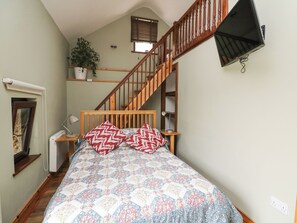 Un dormitorio con cama de madera, una mesita de noche, una lámpara de escritorio, una planta en maceta, una ventana con persianas y una escalera de madera.
