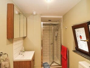 Un baño con tocador de madera, cabina de ducha de vidrio y un inodoro con un ventanal decorativo.
