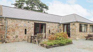 A stone building with a gravel courtyard, wooden chairs, and a flower bed. - Swallow's Nest (Tacumshane)