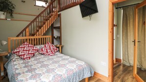 A bedroom with a wooden bed, a staircase, a TV mounted on the wall, and a door leading to another room. - Swallow's Nest (Tacumshane)
