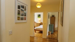 A hallway with wooden flooring, a framed picture on the wall, a bed in the adjacent room, and a cabinet. - Rowantree (Killarney)