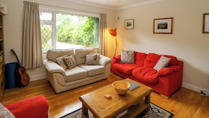 A living room with a beige sofa, a red sofa, a wooden coffee table, and a large window with curtains. - Rowantree (Killarney)