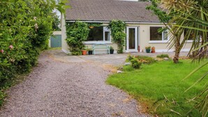 A house with a gravel driveway leading to a front door, surrounded by greenery and potted plants. - Rowantree (Killarney)