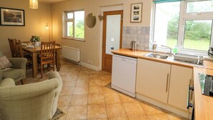A kitchen with a dishwasher, a sink, and a window. There is a dining table with chairs and a lamp. - Rowantree (Killarney)