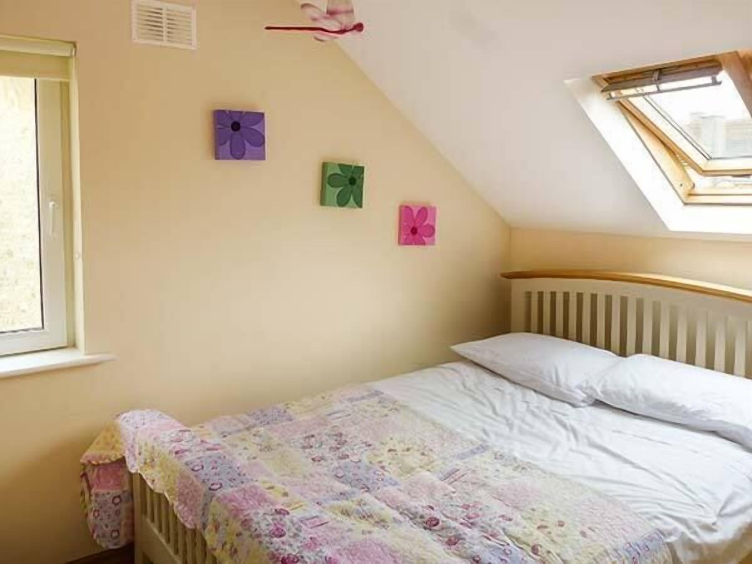 A bedroom with a sloped ceiling, a skylight, a bed with a floral bedspread, and three wall-mounted flower paintings.