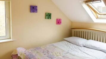 A bedroom with a sloped ceiling, a skylight, a bed with a floral bedspread, and three wall-mounted flower paintings.