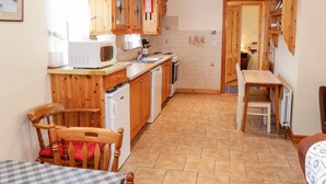 A compact kitchen with wooden cabinets, a microwave, a sink, and a dining area with a table and chairs. - At the Crossroads (Louisburgh)
