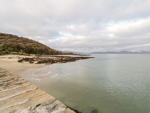 Een kustlandschap met een rotsachtige kustlijn, een zandstrand en een stenen pier die in kalm water uitloopt.