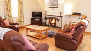 A cozy living room with leather sofas, a fireplace, and a television. - At the Crossroads (Louisburgh)
