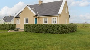 A two-story house with a grey roof, beige walls, and a green door.