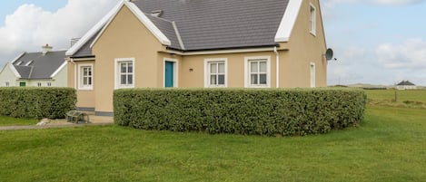 A two-story house with a grey roof, beige walls, and a green door.