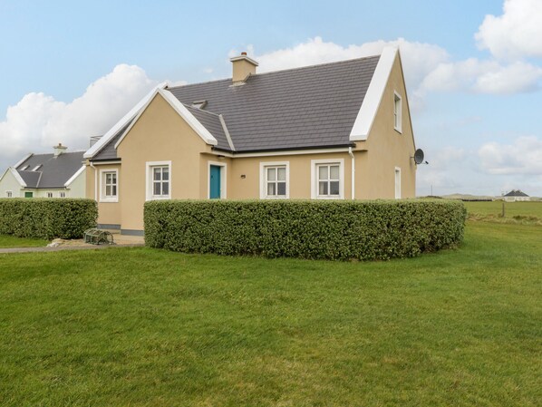 A two-story house with a grey roof, beige walls, and a green door.