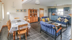 A spacious living area with a high ceiling, a dining table with chairs, a sofa with cushions, and a kitchen area with blue cabinets.