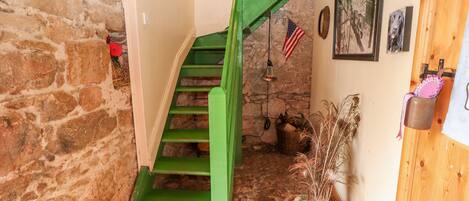 Una escalera estrecha con barandillas verdes que da a un piso de madera.