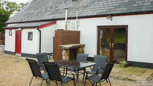 A building with a white exterior and a red door, a stone bench, and a table with four chairs. - Cookies Cottage (Ballyshannon)