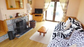 A cozy living room with a fireplace, a sofa, a television, and a wooden bench. - Cookies Cottage (Ballyshannon)