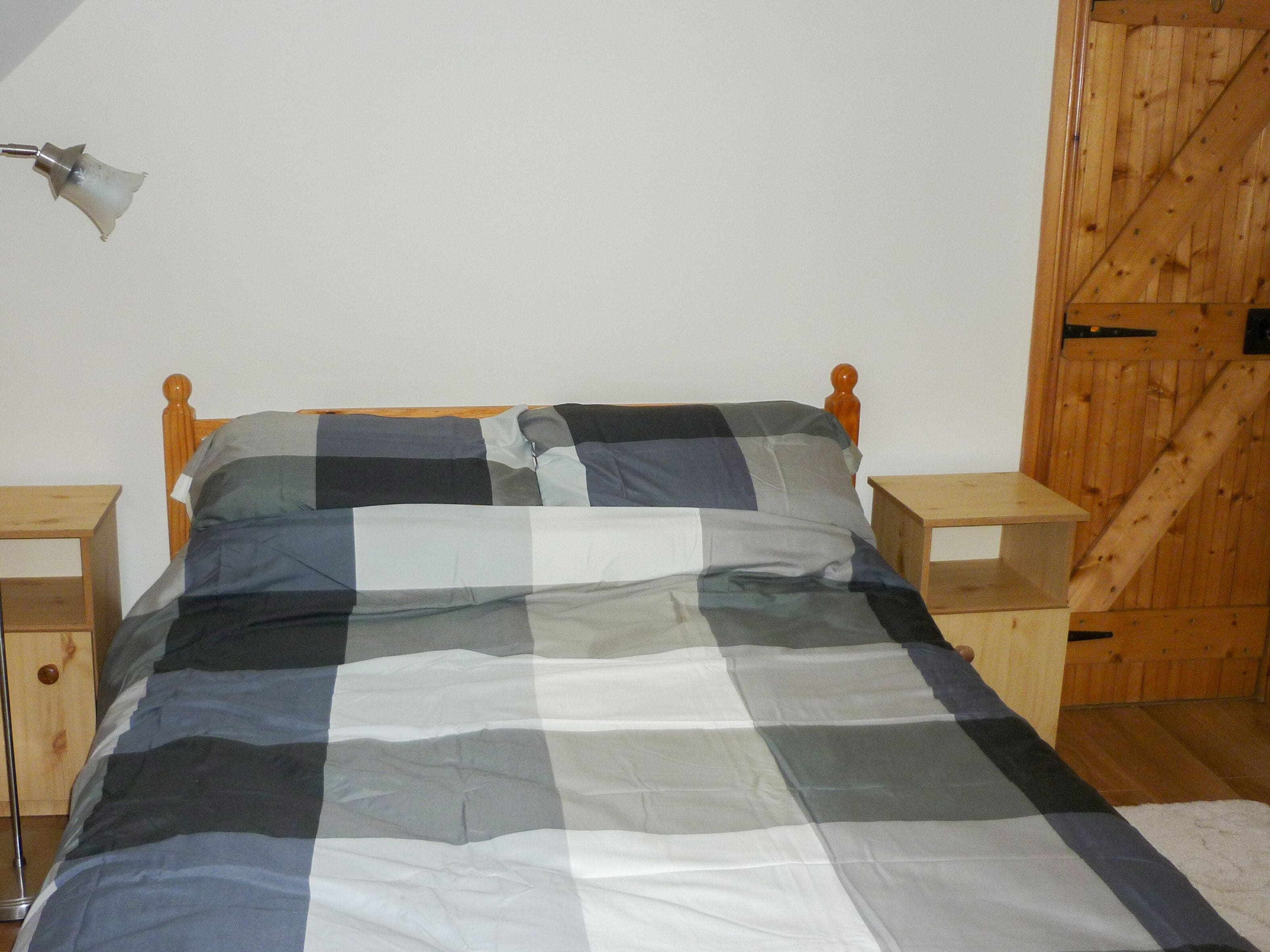 Ein Bett mit karierter Bettdecke in einem Zimmer mit Holzwänden und einem hölzernen Kopfende.