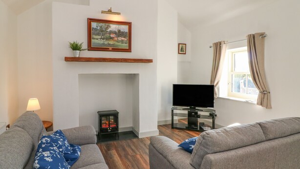 Una sala de estar con chimenea, televisor y dos sofás grises con cojines azules estampados.