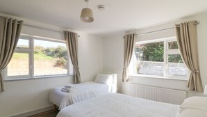 Un dormitorio con dos camas, cortinas color crema, una ventana y un radiador.
