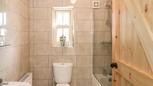 Un baño con inodoro, una ventana con flores, ducha y puerta de madera.