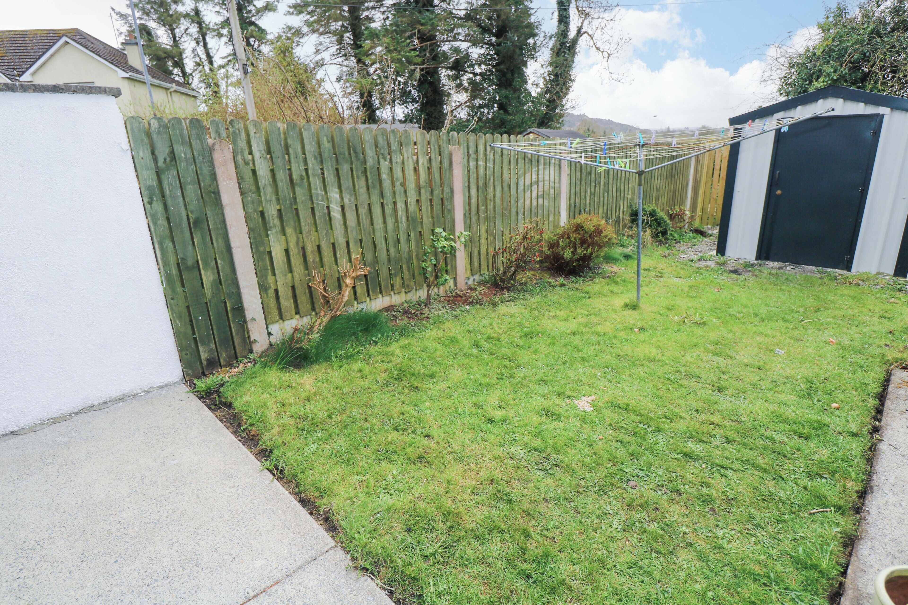 A fenced backyard with a grassy lawn, a shed, and a house in the background.