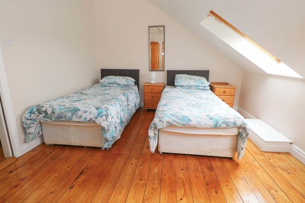 Un dormitorio con dos camas, piso de madera, tragaluz, espejo y mesita de noche.
