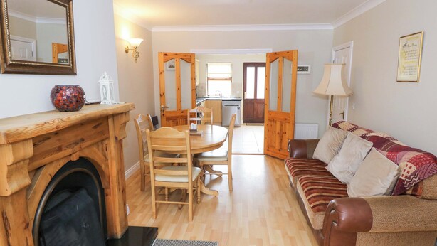 A cozy living room with a fireplace, wooden furniture, and a view into the kitchen. - Aisling (Foxford)