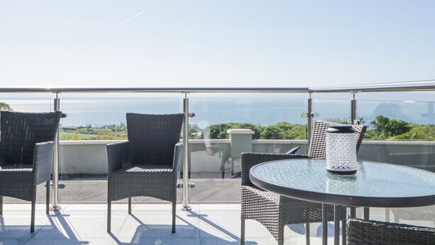 A balcony with wicker chairs and a glass table, overlooking a cityscape. - Tullyally (Moville)