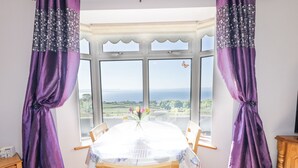 A dining area with a bay window, a table with a floral tablecloth, and purple curtains. - Tullyally (Moville)