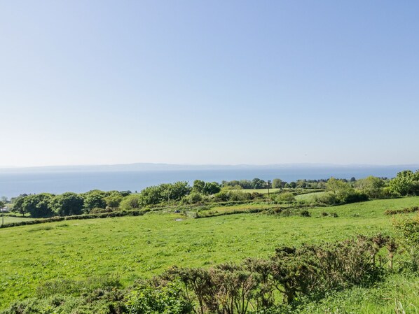 A panoramic view of a green field with a distant view of the sea and hills.