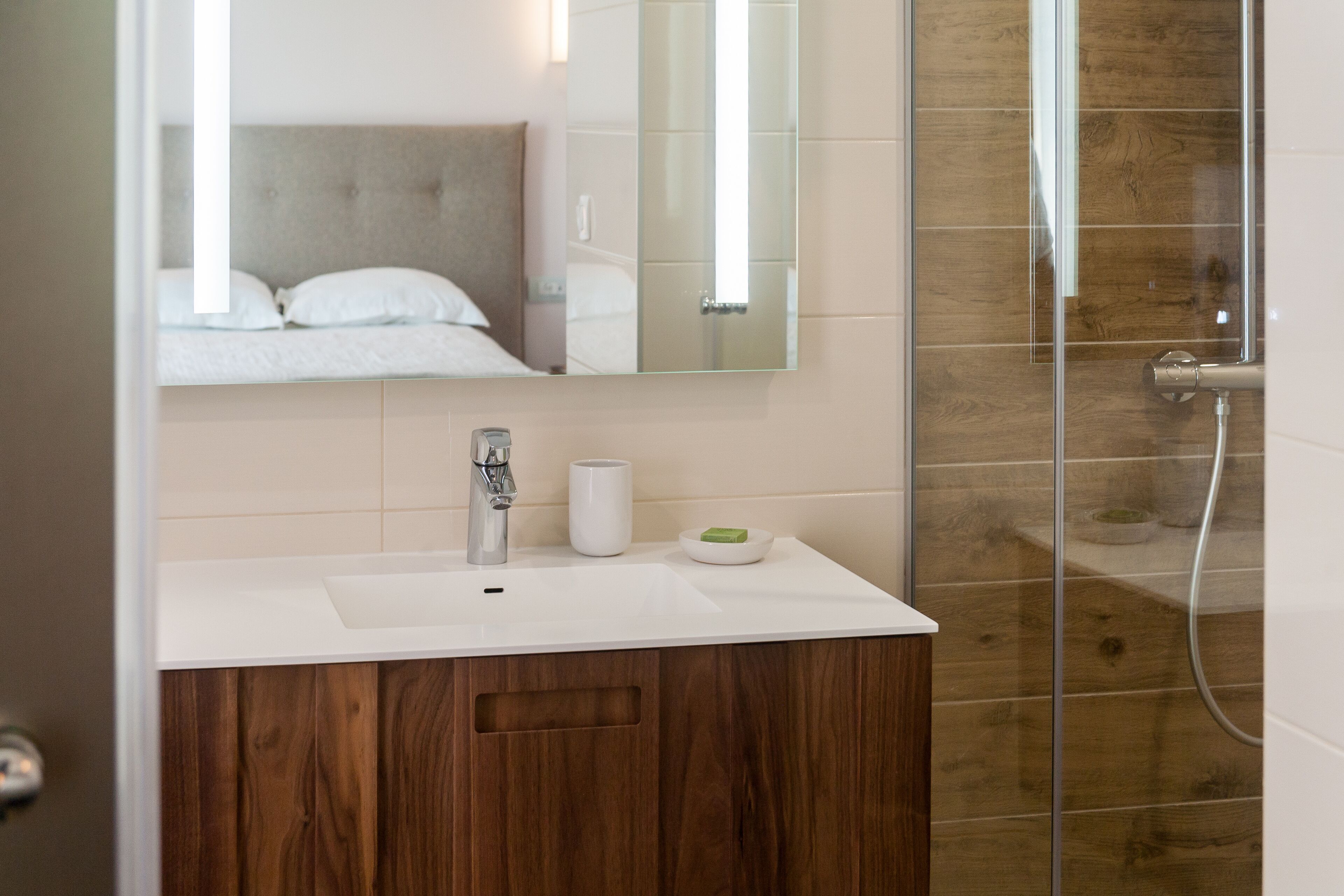 Un baño con lavamanos blanco, espejo, tocador de madera y zona de ducha.