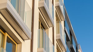 Un edificio de varios pisos con un diseño arquitectónico moderno, con balcones con barandillas de cristal y un cielo azul despejado al fondo.