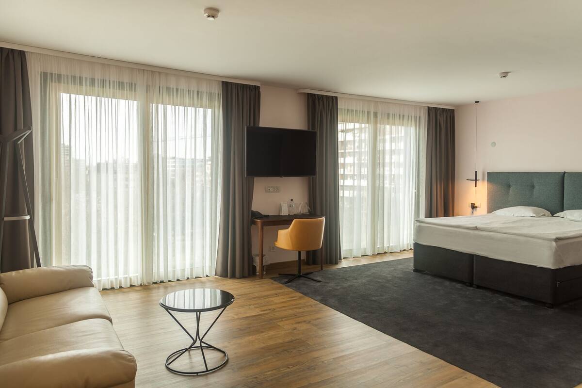 Ein Hotelzimmer mit Bett, Schreibtisch mit Stuhl, Fernseher und Sofa.